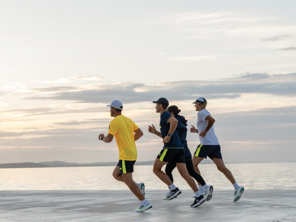 Четирима участника в бягането бягат заедно на плажа.